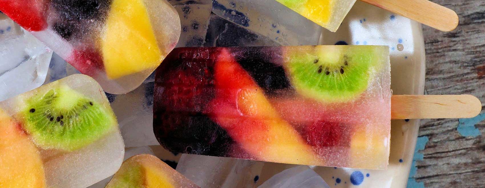 Healthy mixed fruit summer ice pops. Top view in bowl against a rustic blue wood background.